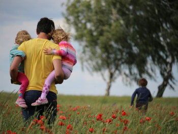 man carrying to girls on field of red petaled flower